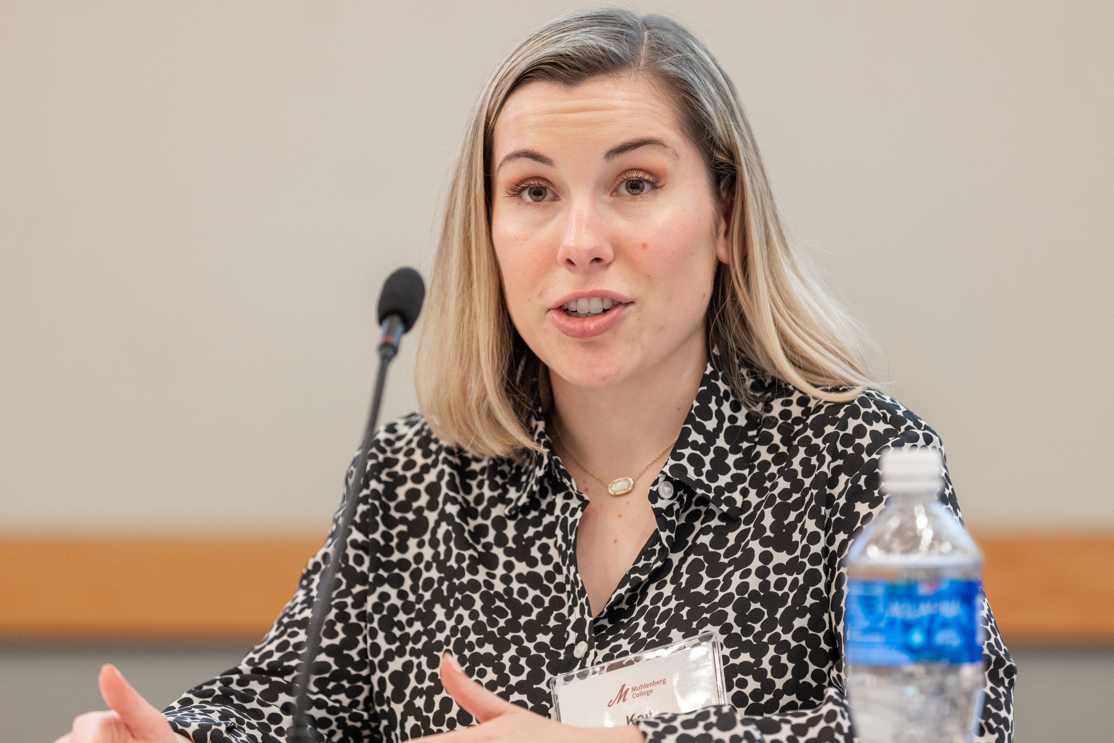 A woman in a black and white blouse speaks at a microphone during a panel discussion.